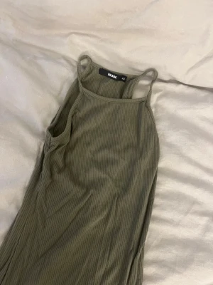 Ribbad khakigrön maxiklänning Bik Bok - Säljer en ribbad maxiklänning från Bik Bok i en snygg khakigrön färg. Klänningen har smala axelband och rak passform, tillverkad i ett mjukt stretchigt material. Perfekt för dig som gillar enkel men trendig stil.