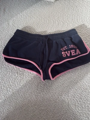 Marinblå shorts från SVEA med rosa kant - Snygga marinblå lågmidjade mini-shorts från SVEA med rosa kantband och snörning i midjan. Perfekta för sommaren.