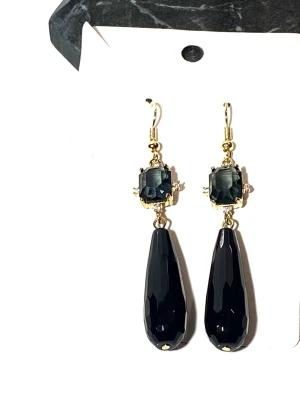 Svarta droppformade örhängen med ädelstenar  - Snygga örhängen med droppformade svarta ädelstenar black onyx länkade med guldpläderad ram och en stor svart ädelsten cubic zirconia och öronkrokar guldplöderade i 24k guld med rostfritt stål i grundmaterial . Längd 8cm