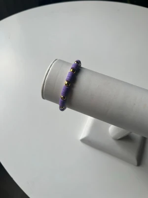Lila armband med guld pärlor - Ett fint somrigt armband som har elastiskt band så det är lätt att ta av och på. armbandet är handgjort.
