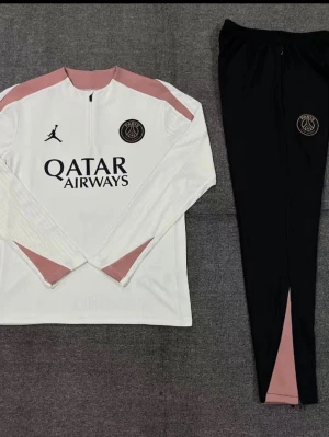 PSG träningsset vit/rosa/svart - Snyggt träningsset från PSG och Jordan med långärmad vit tröja med rosa detaljer och svart byxa med rosa inslag. Tröjan har halv dragkedja, PSG-logga och Jordan-logga samt Qatar Airways-tryck. Byxorna är svarta med PSG-märke och smal passform.