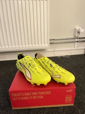 Gula Puma fotbollsskor - Snygga gula fotbollsskor från Puma med svarta och vita detaljer samt klassisk Puma-logga på sidan och tån. Skorna har snörning och är designade för att ge bra grepp på planen. Tillverkade i syntetmaterial för lätt känsla och snabbhet.