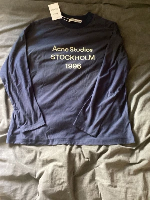 Blå långärmad t-shirt Acne Studios - Snygg mörkblå långärmad t-shirt från Acne Studios med tryck. Lite weird material, inte riktigt bomull som det ska vara!!! Storleken är S men sitter mer som M.