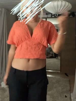 Croppad korall omlottopp - Säljer en croppad topp i en härlig orange färg med omlott-design och v-ringning. Toppen har korta ärmar och ett strukturerat, lätt skrynkligt material som ger en cool look. Perfekt för dig som vill sticka ut lite extra.