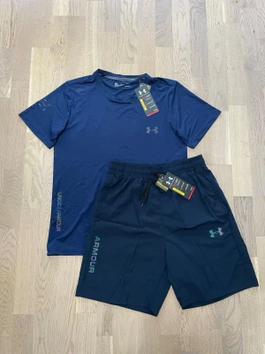 Under Armour set (T-shirt + shorts) – Helt nya med tags - Snyggt och sportigt set från Under Armour med t-shirt och matchande shorts. Perfekt för gym, träning eller vardag.  Båda plaggen är helt nya med tags, aldrig använda. Lätt och bekvämt material med reflexdetaljer – perfekt för både träning och stil.  ✔️ Skick: Helt nya (med tags) ✔️ Set: T-shirt + shorts ✔️ Passform: Sportig och bekväm M/S ✔️ Perfekt för gym, löpning eller vardag och perfekt för sommaren!  Riktigt clean set 🔥