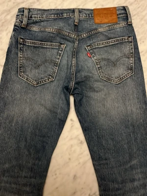 Levi's blå raka jeans - Klassiska blå jeans från Levi's med raka ben och snygg slitning. Jeansen har fem fickor, kontrastsömmar och den ikoniska läderpatchen bak i midjan. Tillverkade i slitstark denim med en cool vintagekänsla.