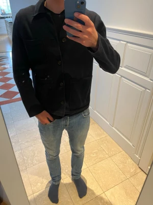 Mörkblå overshirt med fickor - Stilren mörkblå overshirt med tre framfickor och knäppning framtill. Klassisk krage och raka ärmar. Tillverkad i ett mjukt, tjockare tyg som ger en avslappnad look. Perfekt att bära över en t-shirt eller skjorta. Nypris 2299. Storlek xs men passar S