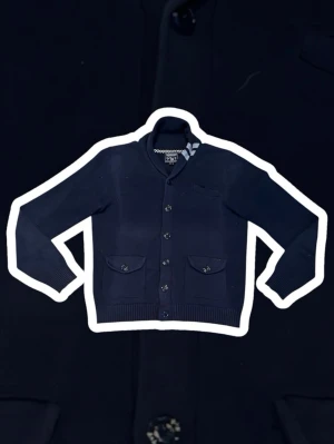 Woolrich cardigan - Stilren mörkblå kofta från GANT med knäppning framtill och två fickor med lock. Tröjan har ribbade muddar vid ärmslut och nederkant samt en liten bröstficka. Perfekt för en klassisk och avslappnad look.