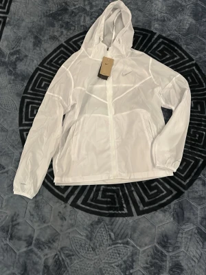Nike Miller - Pris kan diskuteras. Snygg vit vindjacka från Nike med dragkedja framtill och justerbar huva. Jackan har lång ärm, elastiska muddar och en diskret Nike-logga på bröstet. Tillverkad i lätt och tunt material som passar perfekt för blåsiga dagar.