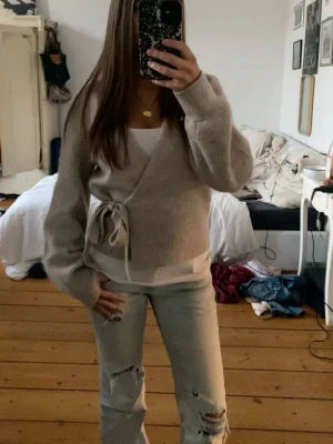 Beige omlottkofta med knytband - Snygg beige omlottkofta med knytband i midjan och långa ärmar. Koftan har en mjuk och fluffig känsla, perfekt för lager på lager. Passar till både jeans och kjol för en chill look.