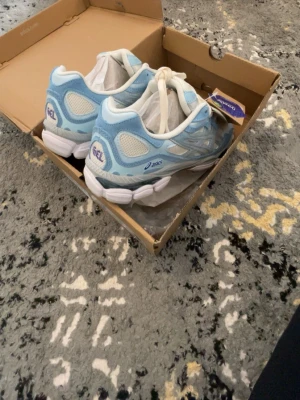 Asics GEL sneakers ljusblå vita - Säljer ett par fräscha Asics GEL sneakers i ljusblått och vitt. Skorna har meshpaneler för bra ventilation, klassisk Asics-logga på sidan och GEL-dämpning i sulan. Perfekta för dig som gillar sportig stil och bekväma skor.