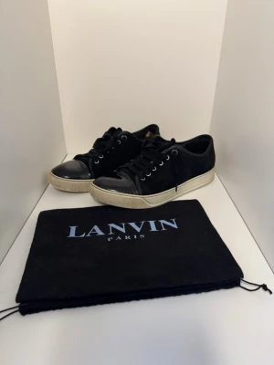 Svarta Lanvin sneakers i mocka och lack - Snygga svarta sneakers från Lanvin med ovandel i mocka och tåparti i blankt lack. Skorna har vita, rejäla gummisulor och svarta skosnören. Klassisk låg modell som passar till det mesta. Medföljer original dustbag. 
