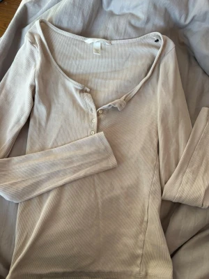 Beige ribbad långärmad topp H&M - Långärmad topp från H&M i en ljus beige nyans. Toppen är ribbad, har v-ringning med knappar framtill och är tillverkad i mjuk bomullsmix. Perfekt för lager på lager och enkel att styla till olika looks.