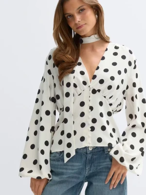 Vit prickig blus med knytband - Slutsåld viral och trendig blus från Gina! Helt oanvänd med lappar kvar‼️‼️Trendig vit blus med svarta stora prickar och v-ringning. Blusen har långa, vida ärmar och ett dekorativt knytband vid halsen. Tillverkad i ett lätt, flygigt material som ger en snygg siluett. Perfekt för dig som gillar retrovibbar och statementplagg.