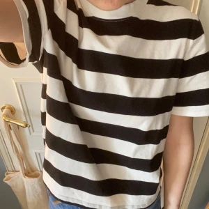 Randig svartvit t-shirt - Säljer en klassisk svartvit randig t-shirt med breda horisontella ränder. T-shirten har rund halsringning och korta ärmar. Perfekt till jeans eller shorts för en enkel och stilren look.