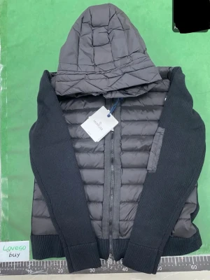 Moncler cardigan nfc - Snygg svart pufferjacka från Moncler med quiltad front och huva. Jackan har stickade ärmar och rygg, dragkedja framtill och en ficka med dragkedja på ärmen. Perfekt för kalla vinterdagar och har klassisk Moncler-logga på axeln. Storlek m men passar oxå för s