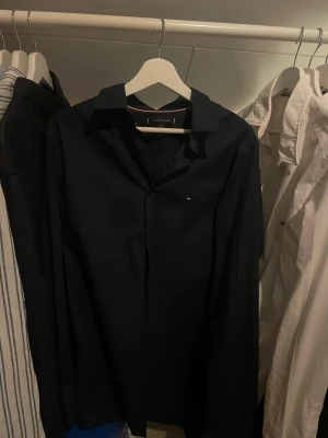 Marinblå skjorta | Tommy Hilfiger - Snygg marinblå skjorta från Tommy Hilfiger. Skjortan är i slim fit och storlek L. Mycket bra skick och riktigt snygg till sommaren! Skriv privat för fler bilder eller funderingar!