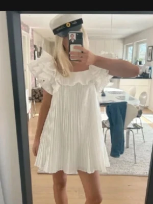 Vit kort plisserad klänning med volang - Säljer en superfin vit kort klänning med plisserad kjol och stora volangärmar. Klänningen har en luftig passform och fyrkantig ringning, perfekt för student eller sommarens alla tillfällen. De två sista bilderna är mina!💓💓