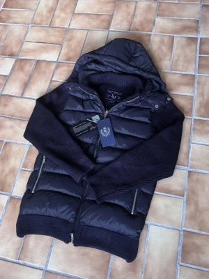 Marcél Classic Hybridjacka – Midnight Navy | Avtagbar Luva | Ny Med Prislapp - Ny med prislapp — Marcél Classic i djup midnattsblå med quiltad pufferkropp och stickade ärmar. Avtagbar luva och lyxiga microfleecefickor som håller händerna varma — detaljer som gör skillnad. Perfekt för både höst/vinter och kyliga vårdagar — en jacka du bär hela säsongen. Finns i flera storlekar — skriv din längd och vikt så hjälper jag dig hitta den perfekta passformen! Säljer direkt för ett bättre pris än butik. 📦 Spårad frakt, väl förpackad.