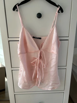 Ljusrosa linnetopp från Gina Tricot - Supersöt ljusrosa linnetopp från Gina Tricot med tunna axelband och snygg snörning framtill. Toppen har en lätt glansig finish och är perfekt för sommar och vår. Materialet känns mjukt och svalt mot huden. Använd 1 gång💗