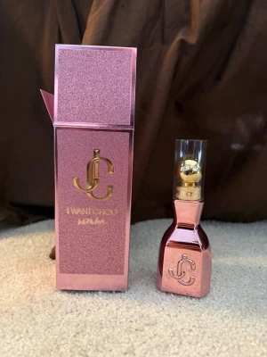Jimmy Choo I Want Choo Parfym - Lyxig parfym från Jimmy Choo, 'I Want Choo', i en snygg rosa metallicflaska med gulddetaljer och genomskinligt lock. Förpackningen är glittrig rosa med guldfärgat JC-monogram. Perfekt för dig som gillar eleganta och trendiga dofter.