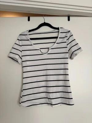 Randig ribbad topp med rundringning - Säljer en vit ribbad topp med svarta horisontella ränder och rundringad hals. Toppen har korta ärmar och är i ett mjukt, stretchigt material som sitter snyggt på kroppen. Perfekt till jeans eller kjol!