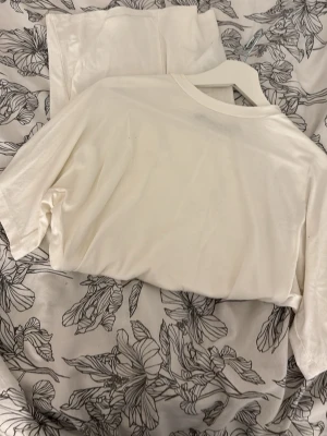 Vit enkel kort klänning - Minimalistisk vit kort klänning i mjukt material med rund hals och korta ärmar. Perfekt för en avslappnad och stilren look. Klänningen har en rak passform och är utan synliga detaljer eller mönster.