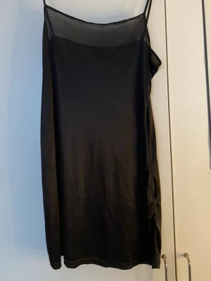Svart nattlinne med tunna axelband - Svart nattlinne med tunna axelband och rak passform. Materialet ser ut att vara mjukt och lätt, perfekt för att chilla hemma. Nattlinnet har en enkel design utan mönster och är lite glansigt i tyget. Har inga lappar, köptes secondhand. Känns som ett s/m ungefär