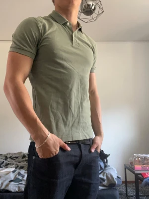 Grön piké t-shirt med krage - Snygg grön piké t-shirt med klassisk krage och korta ärmar. Modellen är slim fit och har två knappar vid halsen. Perfekt till jeans eller shorts för en clean och enkel stil.