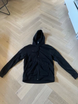 Svart ziphoodie från Hugo boss - Säljer en svart hoodie med dragkedja och huva. Hoodien har långa ärmar, två fickor framtill och en enkel design utan synliga loggor. Perfekt för dig som gillar en clean och stilren look. Materialet ser ut att vara mjukt och bekvämt.