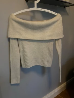 Off shoulder stickad tröja cremevit - Trendig off shoulder stickad tröja i cremevit färg. Ribbstickad med bred krage som vilar över axlarna och långa ärmar. Perfekt för dig som vill ha en stilren och modern look. Mjuk och skön, passar till många outfits.