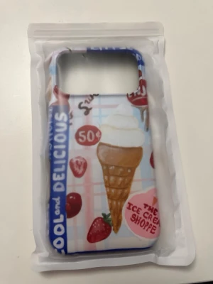 Mobilskal med glass och jordgubbar - Färgglatt mobilskal med motiv av en glasstrut, jordgubbar och text som 'COOL and DELICIOUS' och 'THE ICE CREAM SHOPPE'. Skalets bakgrund har rutigt mönster i pastellfärger och detaljer i blått, rött och rosa. Skalet är MagSafe, och är gjort för iPhone 17 PRO Max, det är ifrån märket inside & out och säljs pga att jag råkat köpa dubbelt. Original pris är 374 kr
