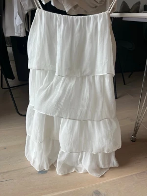 Vit klänning från Vila - Säljer en superfin vit klänning med tunna axelband och flera lager volanger. Klänningen är kort och har en luftig, flowy känsla som passar perfekt till sommaren. Materialet känns lätt och svalt, troligen polyester eller liknande. Perfekt för dig som gillar en romantisk och enkel stil. PERFEKT TILL STUDENTEN. Passar mig som bär S och även M