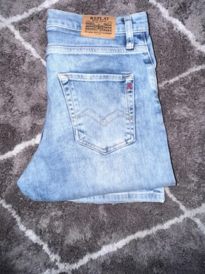 Ljusblå jeans från Replay - Säljer ett par ljusblå jeans från Replay med klassisk femficksmodell och snygg tvätt. Jeansen har en patch med Replay-logga bak i midjan och diskret broderad detalj på bakfickan. Tillverkade i mjukt denimtyg som ger en avslappnad look.