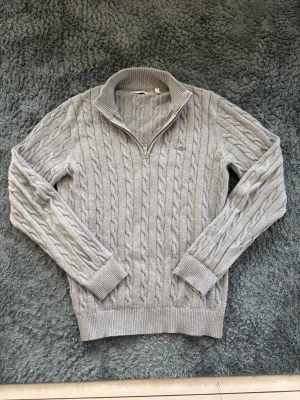 Ljusgrå kabelstickad tröja med halvzip - Säljer denna feta ljusgrå kabelstickade tröjan med halv dragkedja och krage. Skicket är 10/10. Använd en gång. Tröjan är storlek 176 cm/ 16 år. Men passar som en S. Om du har några frågor är det bara att skriva, pris kan såklart diskuteras! 