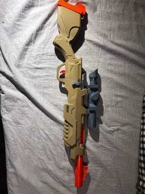 Leksaksgevär MXM-018 Ambush Rifle - Säljer ett leksaksgevär i plast, modell MXM-018 Ambush Rifle. Geväret är beige med orange detaljer och har ett grått kikarsikte på ovansidan. Perfekt för lek och äventyr med kompisarna.