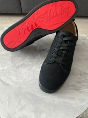 Christian Louboutin Skor Loubs  - Stilrena svarta sneakers från Christian Louboutin med klassisk röd sula och guldfärgad logga på insidan. Skorna har en låg profil, rund tå och är tillverkade i mocka med matchande svarta skosnören. Perfekta för dig som gillar exklusiv streetstyle.