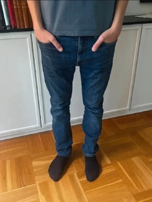 Mörkblå slim fit jeans Tommy Hilfiger - Snygga mörkblå slim fit jeans med klassisk femficksdesign och lätt slitning. Jeansen har raka ben och normal midja, perfekt för dig som gillar en modern och stilren look. Materialet är denim och passar till många olika outfits.
