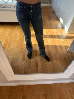 Blå bootcut jeans med klassisk look - Säljer ett par blå bootcut jeans med klassisk femficksdesign och knappgylf. Jeansen har en lätt tvättad finish och sitter snyggt på höften. Perfekta för dig som gillar en tidlös och avslappnad stil.