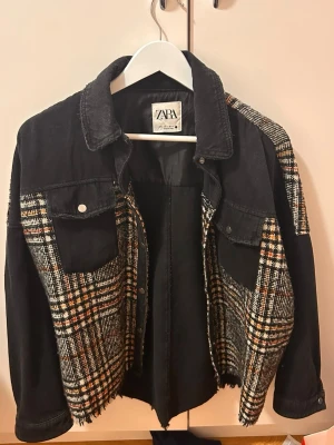 Svart och rutmönstrad jeansjacka Zara - Trendig svart jeansjacka från Zara med rutmönstrade paneler. Jackan har två bröstfickor med knapp, klassisk krage och rå kant nedtill för en liten edgy look. 
