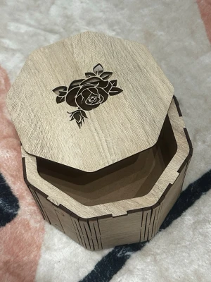 Oktagonformad smyckesask i trä - Snygg oktagonformad smyckesask i ljust trä med ett graverat ros-motiv på locket. Perfekt för att förvara ringar, örhängen eller andra småsaker. Asken har en stilren och naturlig look som passar in i de flesta rum.