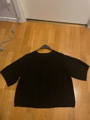 Svart stickad tröja från 157 - En enkel och stilren svart stickad tröja från 157 med rund halsringning och halvlånga ärmar. Tröjan har en rak passform och är perfekt för lager på lager. Klassisk design som funkar till det mesta.