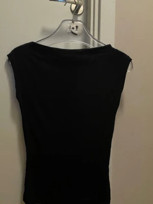 Svart ärmlös topp från Nelly - Säljer en svart, enkel och stilren ärmlös topp från Nelly. Toppen har en tight passform och är tillverkad i ett mjukt material som känns skönt mot huden. Perfekt att matcha med jeans eller kjol för en clean look.