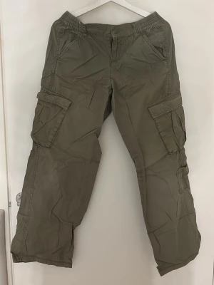 Olivgröna cargobyxor med fickor - Säljer ett par olivgröna cargobyxor med flera stora fickor på sidorna och avslappnad passform. Byxorna har resår i midjan och är tillverkade i ett lätt bomullstyg. Perfekta för en chill och casual stil.