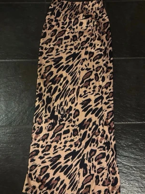 Långkjol - Säljer en snygg långkjol med leopardmönster i beige, svart och brunt. Kjolen har elastisk midja och är gjord i ett mjukt, lätt material som ger en skön känsla. Perfekt för dig som vill sticka ut med ett trendigt djurmönster.