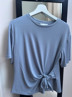Ljusblå topp med knyt framtill - En stilren ljusblå topp med korta ärmar och rund halsringning. Super fin till ett bar jeans eller en kjol. Använd två gånger och köpt i somras.