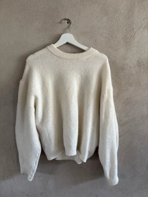 Vit oversized stickad tröja - Mysig oversized stickad tröja i offwhite med rund halsringning och ribbade muddar vid ärmslut och nederkant. Tröjan har en avslappnad passform och är tillverkad i ett mjukt, fluffigt material som känns skönt mot huden.