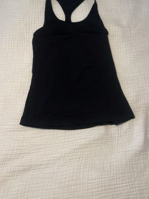 Svart träningstopp med brottarrygg - Säljer en svart träningstopp från Xercise med brottarrygg. Toppen är ärmlös och har en tight passform som passar perfekt till gymmet eller löprundan. Materialet är mjukt och stretchigt för maximal komfort.