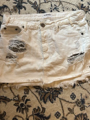 Vit slitna shorts från OneTeaspoon - Vit kort jeanskjol från OneTeaspoon med slitna detaljer och fransad nederkant. Klassisk femficksmodell med knapp och dragkedja framtill. Det är i storlek 27. De är i fint skick med inga hål eller fläckar så den säljs för den inte passade mig .💕