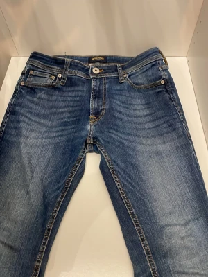 Blå Jack & Jones  jeans SKINNY/LIAM - Säljer ett par blå skinny jeans från Jack & Jones  med klassisk femficksdesign och snygga slitningar. Jeansen har smal passform och kontrastsömmar, perfekta för en trendig vardagslook. Materialet är mjukt denim med stretch för extra komfort.